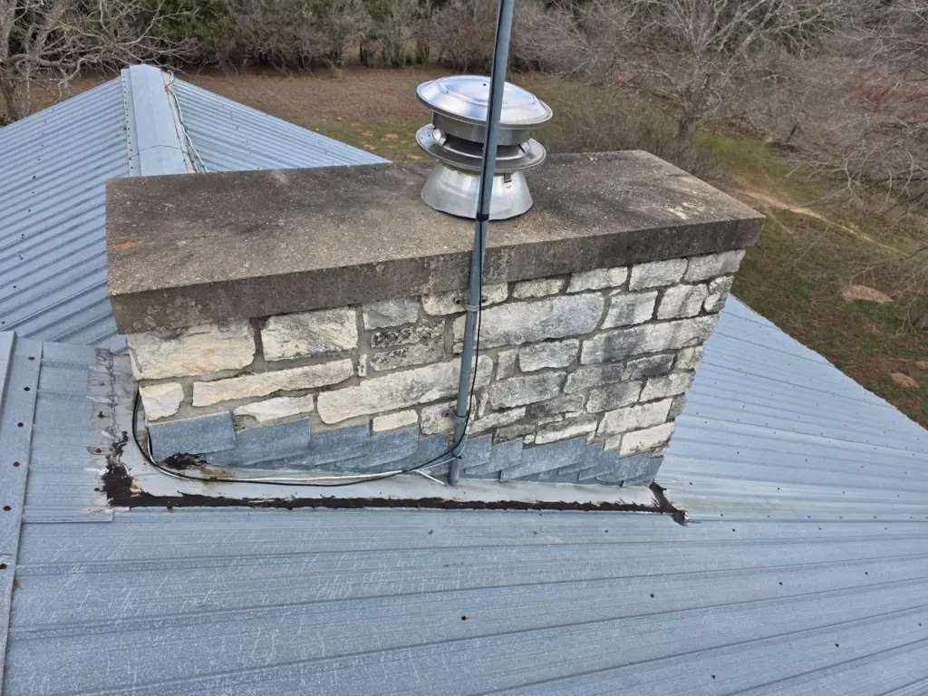 Old chimney flashing sealed with tar on the R-panel roof