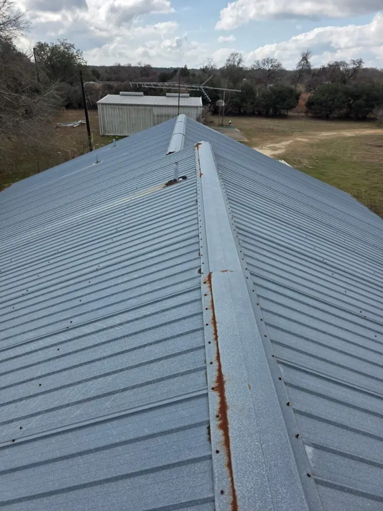 Rusted ridge cap and exposed fasteners on the old R-panel roof