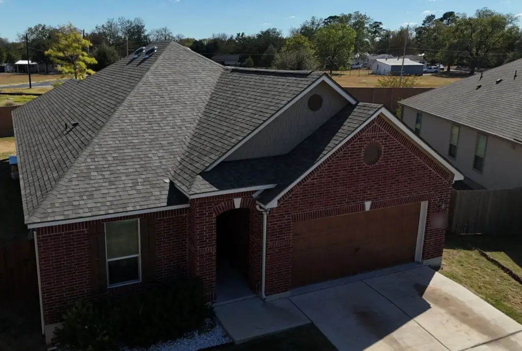 Front of the red brick home showing the new Driftwood shingle roof over the arched entry and garage